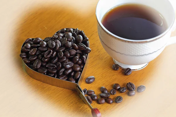 在木桌上的咖啡杯子和咖啡豆心的形状 — 图库照片