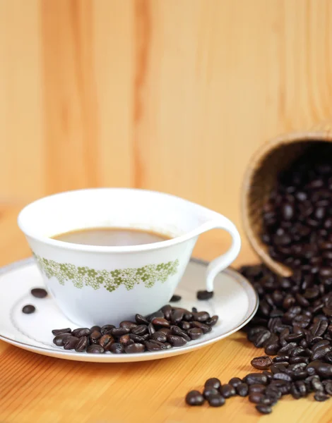Šálek kávy a kávových zrn na dřevěný stůl — Stock fotografie