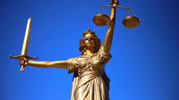Bronzestatue Der Gerechtigkeit Mit Einem Schwert Vor Blauem Hintergrund lizenzfreie Stockbilder