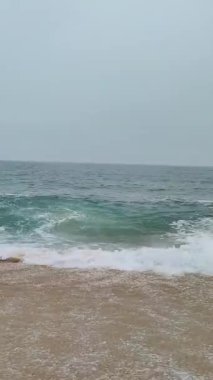 Waves of the Atlantic ocean crushing on the beach in Nazare, Portugal short vertical video. 