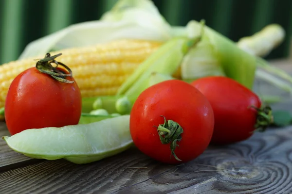 Τρεις κόκκινες ντομάτες cherry με ένα καλαμπόκι στάχυ και δύο λοβούς μπιζελιών — Φωτογραφία Αρχείου