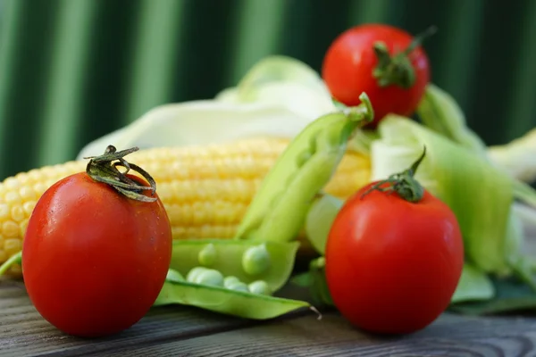 Tres tomates rojos cereza con una mazorca de maíz y dos vainas de guisantes — Foto de Stock