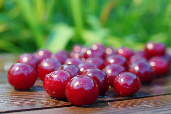 Wet cherry on a wooden plank on a green blurred background — Stock Photo, Image