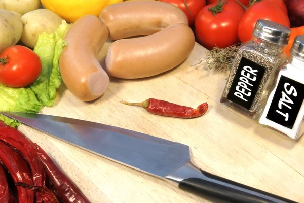 Enchidos crus, legumes e faca de grande chef em tábua de madeira — Fotografia de Stock