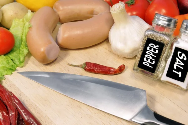 Saucisses crues, légumes et couteau de grand chef sur planche en bois — Photo
