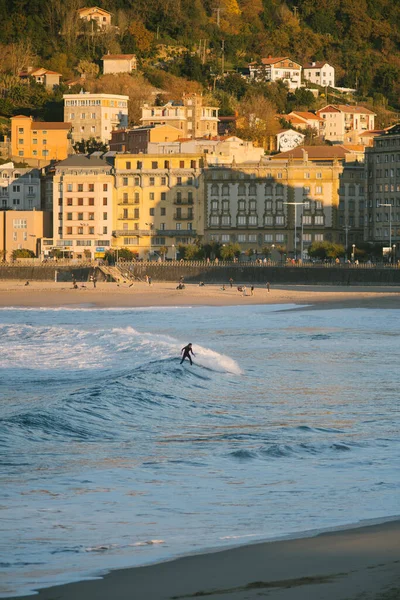 San Sebastian sahilinde gün batımında küçük bir dalgayla kıyıya ulaşan dişi sörfçü.