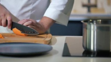 Bir evin ya da restoranın mutfağında yemek pişirmek. Şef bir bıçakla sebze salatası için olgun bir havucu dilimlere ayırır. Lezzetli bir öğle ya da akşam yemeği için malzemeler hazırlanıyor..