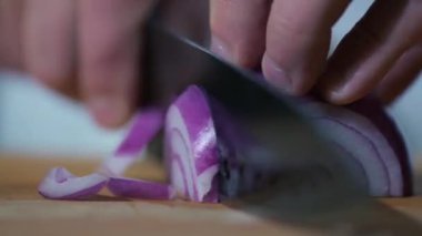 Ev ya da restoranın mutfağında yakın çekim. Tahtadaki şef bıçakla yemek için pembe soğanları dilimlere ayırıyor. Lezzetli öğle ya da akşam yemeği için malzemeler hazırlanıyor..