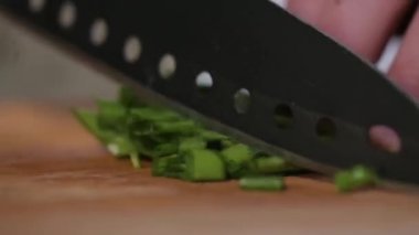 Ev ya da restoranın mutfağında yakın çekim. Tahtadaki şef sağlıklı yemek için taze yeşil soğanları bıçakla kesiyor. Lezzetli öğle yemeği için sebze malzemeleri hazırlıyorum.