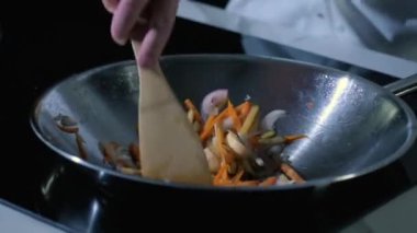 Ev ya da restoranın mutfağında yemek pişirmek. Tavada kızartılmış sebzeler. Şef, klasik tariflere göre Asya mutfağından lezzetli yemekler hazırlar. Adam ahşap kaşıkla malzemeleri karıştırıyor..