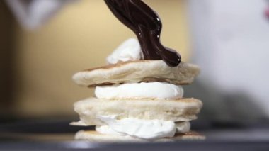 Pişirme krepinin yakın çekimi. Çırpılmış hamur pişirmek lezzetli bir tatlıdır. Şef tatlı tatlıya kaşıktan sıcak çikolata şurubu döker. Kahvaltıda kremalı ve şuruplu taze krep.