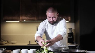 Önlüklü aşçı mutfakta öğle yemeği hazırlıyor. Bir adam lezzetli bir yemek hazırlamak için tavaya sebze parçaları döker..