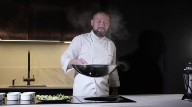 Önlüklü aşçı mutfakta öğle yemeği hazırlıyor. İnsan tüm malzemeleri karıştırmak için tavaya yemek atar. Restoranda akşam yemeği için lezzetli yemekler.