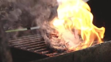 Barbekü dışarıda. Aşçı kömür ızgarasında ateşte et pişiriyor ve ızgarada maşayla biftek pişiriyor. Açık hava yemekleri, barbekü, yaz pikniğinde sokak yemekleri.