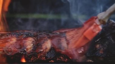 Barbekü pikniği dışarıda. Izgarada ateşte kızartılmış pirzolaların yakın çekimi. Barbekü soslu biftek. Büyük bir arkadaş grubu için yazın leziz ızgara et pişirmek.