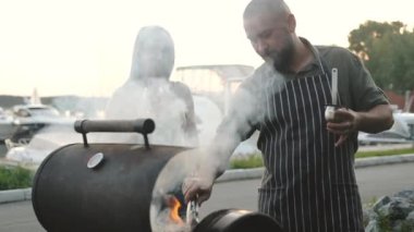 Mutlu adam ve bir kadın ızgarada etli biftek hazırlıyorlar. Arkadaşlar piknikte dinleniyorlar ve temiz havada barbekü hazırlıyorlar, bira içip sohbet ediyorlar..