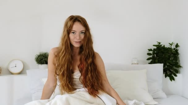 一个穿着睡衣 躺在枕头和毛毯中间 躺在白色卧室里的快乐微笑的女人的画像 早上醒来的时候 — 图库视频影像