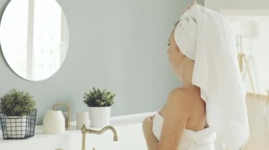 Mutlu çekici kadın sabah banyo aynasına bakar, sağlıklı genç bayan duş aldıktan sonra kafasına havlu sarar. sağlıklı cilt bakımı kavramı