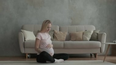 Hamile ve güzel bir kadın dairenin içinde oturmuş karnını okşuyor. Bebeğin doğmasını bekliyorum. Yavrular için genç ebeveynlere bakmak