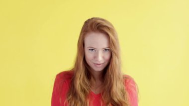 Güzel, beyaz, ciddi, kızıl saçlı kadın izole edilmiş sarı arka planda kameraya dikkatlice bakıyor.