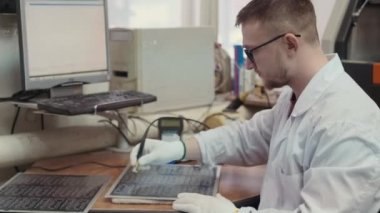 Operatör kalite kontrolü yapıyor. Modern üretimde üniformalı işçiler yüksek teknolojili ekipmanlar üzerinde çalışıyorlar. Dijital üretimde deneyimli bir mühendis yazdırılmış devre kartını kontrol eder