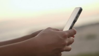 Genç kadın sosyal medya sohbeti için akıllı telefon kullanıyor. Günbatımı arka planı, hücre bağımlılığı, yeni dönem teknolojisi.