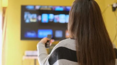 Genç bir kadın akıllı TV uygulamasına göz atıyor, boş zamanlarında kanalları zaplıyor, ev teknolojisi yaşam tarzı...