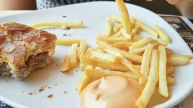 Genç bir kadın fast food restoranında patates kızartması ve hamburger yer, sağlıksız yemekler. 4k
