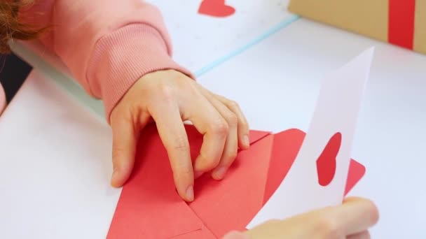 Egy nő Valentin-napi képeslapot tesz piros szívvel borítékba. Gratuláció és ajándék elkészítése ünnepre vagy születésnapra. A szerelem kinyilatkoztatása, a kapcsolat fogalma. Kiváló minőségű FullHD felvételek — Stock videók