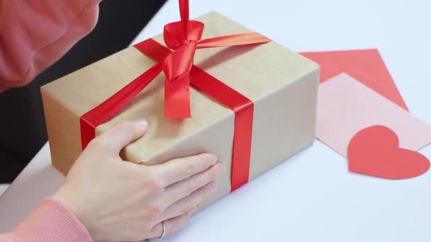 Mujer joven apertura regalo caja regalo presente, desatando cinta roja de San Valentín presente sentado en el interior. Recibe la sorpresa en el aniversario. Declaración de amor, concepto de relación. Imágenes FullHD de alta calidad — Vídeos de Stock