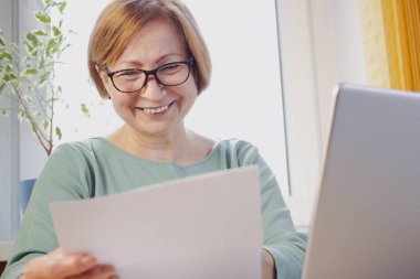 Gözlüklü mutlu orta yaşlı kadın kağıt belgeler okuyor ya da evde dizüstü bilgisayarla oturan bir arkadaştan posta mektubu alıyor. Evrak işlerinden hoşlanmayan banka bildirisi veya yazışmaları reddediliyor