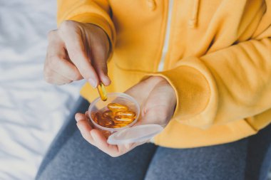 Woman taking omega 3 fish oil capsule from plastic box.Food supplements and vitamins concept.Fish oil in jelly-like transparent yellow pills.Everyday morning routine.Diet nutrition supplement concept