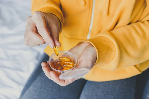 Plastik kutudan Omega 3 balık yağı kapsülü alan kadın. Besin takviyeleri ve vitamin konsepti. Şeffaf sarı haplar içinde balık yağı.