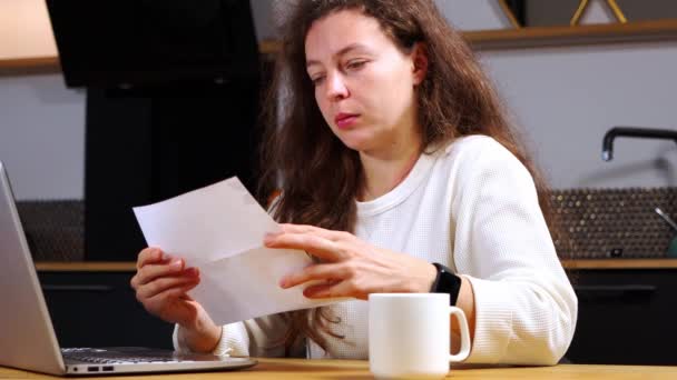 Shocked worried young brunette woman reading paper document or postal letter feeling frustrated by unexpected bad news sitting at home indoors. Received bank account balance, fine notice, bankruptcy — Stock videók