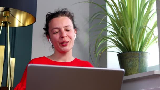 Beautiful young business woman wearing headphones communicating by video call, sitting indoors. Speaking looking at laptop computer, online conference distance office chat, virtual training concept — Stock videók