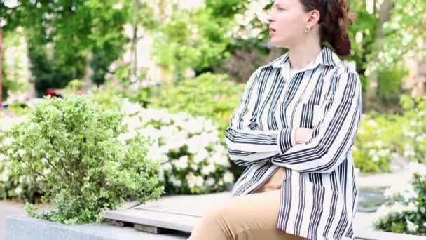 Mujer joven nerviosa molesta esperando a alguien sentado en el hermoso jardín floreciente al aire libre. Mirando su reloj de pulsera preocupado, volviéndose impaciente. Expresión facial de la emoción humana, reacción lenguaje corporal — Vídeo de stock