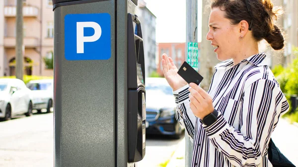 Angry young woman pay for ticket by credit card in parking meter, looking confused at terminal standing on street outdoors. Debt problems, failed transaction, error of electronic payment transaction.