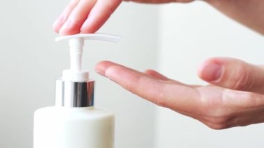 Hands applying sanitizer gel. Pushing dispenser and antibacterial liquid soap squeezed out to palm, closeup on white room background. Washing at bathroom, using soft gel for advanced skin care. 