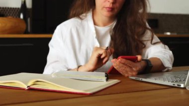 Accounting. Cropped young brunette woman using phone count amount payable on digital calculator, pay domestic bills fees online. Planning monthly budget at home office.Unsatisfied of increase in costs