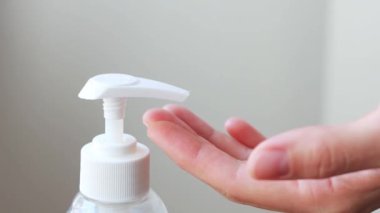 Woman hands pushing dispenser and antibacterial liquid soap squeezed out to palm, closeup on white bathroom background. Washing using soft gel for advanced skin care. Bacteria and virus protection.