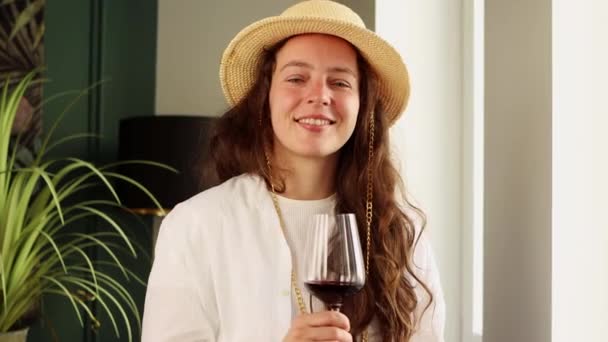 赤ワインアルコールとワイングラスを保持夏のわら帽子で幸せな若い美しい女性は カメラを見て笑って レストランでパーティーで休憩時間を楽しんで 白いシャツを着て リラクゼーションライフスタイル — ストック動画