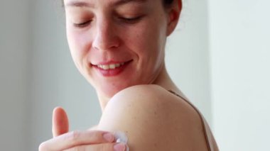 Genç esmer kadın omzuna güneş kremi sürüyor, duştan sonra günlük vücut losyonu yapıyor. Güzellik ve sağlıklı cilt bakımı konsepti. Güneş kremi spa koruması..