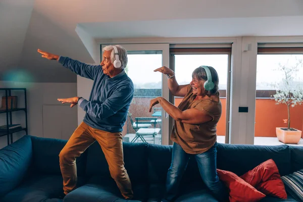 Mutlu yaşlı çift evdeki kanepede müzik dinleyerek dans ediyor.