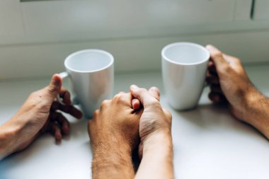 Erkek çift bir fincan kahve ya da çayla el ele tutuşuyor. Ev kafesinde ya da otelde gay dinleniyor.
