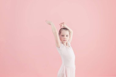 Pembe arka plandaki kameraya bakarken kollarını kaldırmış pembe etekli güzel balerin kızın portresi.