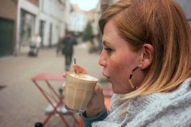 Yakın plan beyaz kadın portresi açık hava kahve masasında rahatlarken macchiato içiyor. 