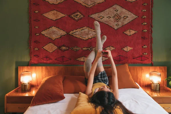 스타킹을 침대에 겨울긴 양말을 소녀가 휴대폰을 사용하여 — 스톡 사진