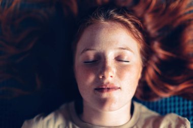 Kafkasyalı kızın yakın plan portresi. Çilli, kızıl saçlı, gözleri kapalı.