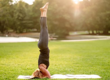 Salamba sirsasana pozisyonunda duran bir kadının yan görüntüsü - atlet gün batımında parkta egzersiz yapıyor - düz bacaklı destekli baş duruşu