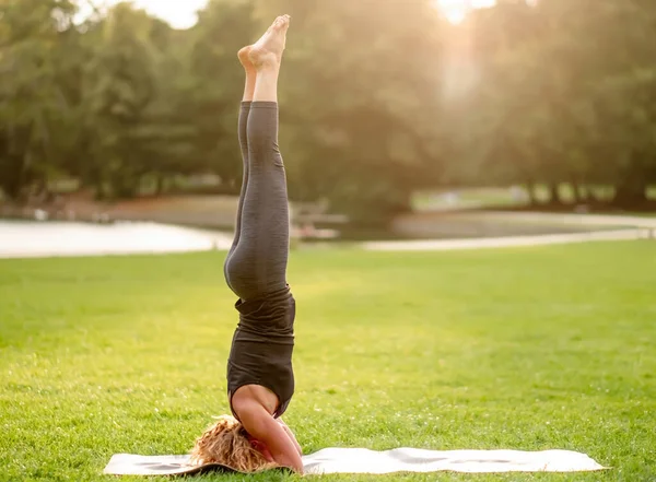 Salamba sirsasana pozisyonunda duran bir kadının yan görüntüsü - atlet gün batımında parkta egzersiz yapıyor - düz bacaklı destekli baş duruşu
